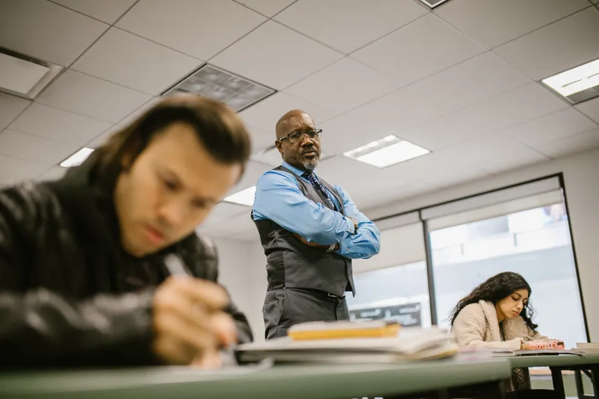 A professor supervises students during an exam, ensuring integrity in a classroom setting.