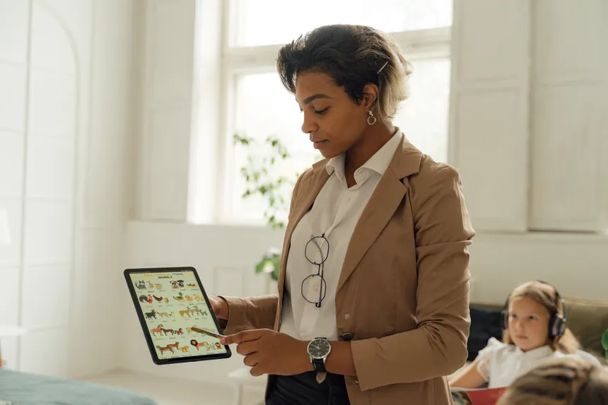 A teacher using a tablet in a bright classroom to explain a lesson to a student.