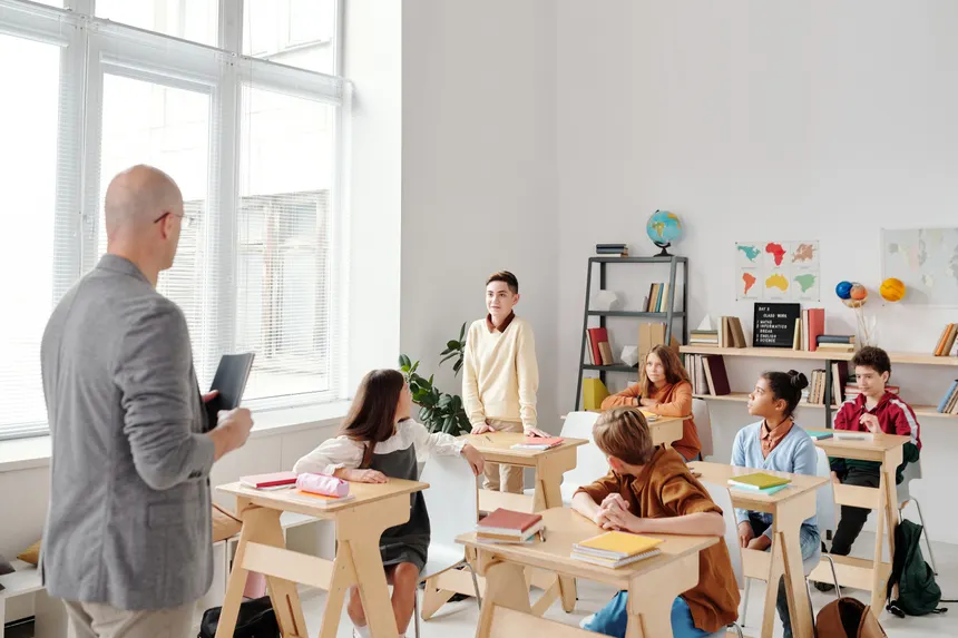 A diverse group of students engaged in learning with a male teacher in a modern classroom setting.