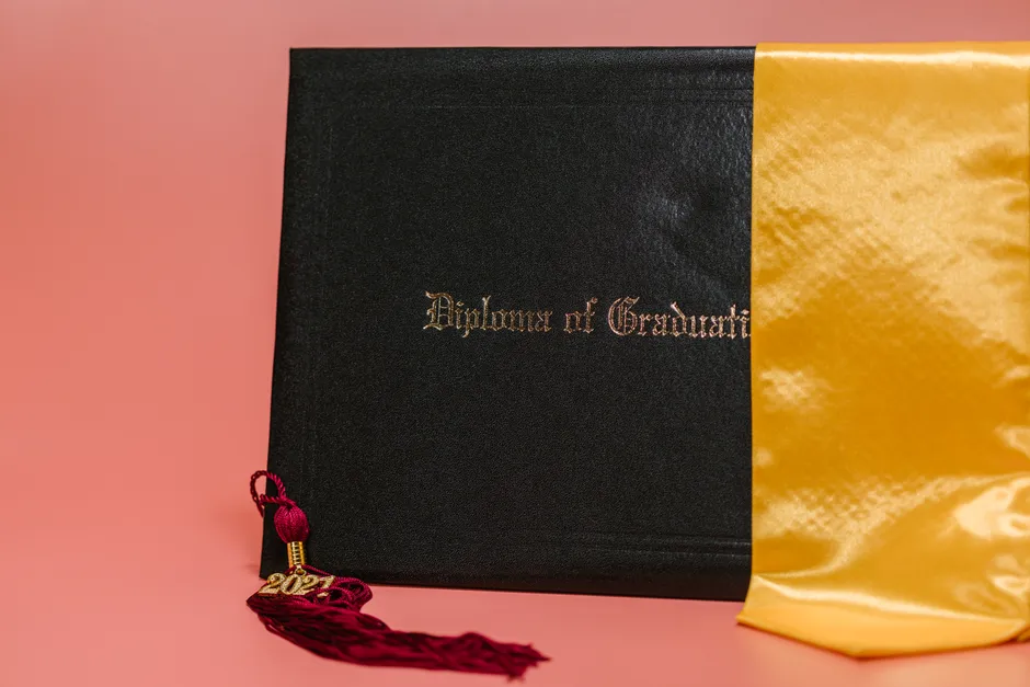 Black diploma with garnet tassel and gold sash symbolizes academic achievement.