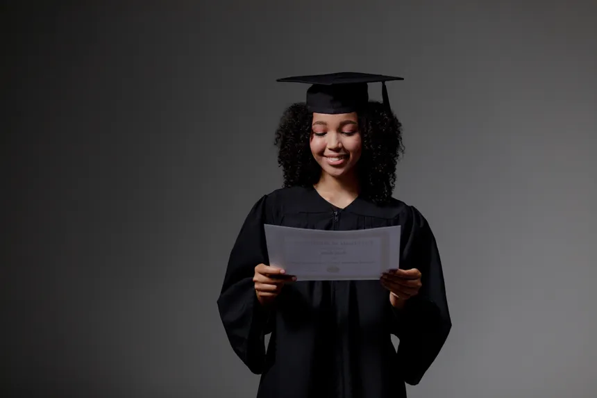 Smiling young woman in graduation gown holding diploma in studio setting.