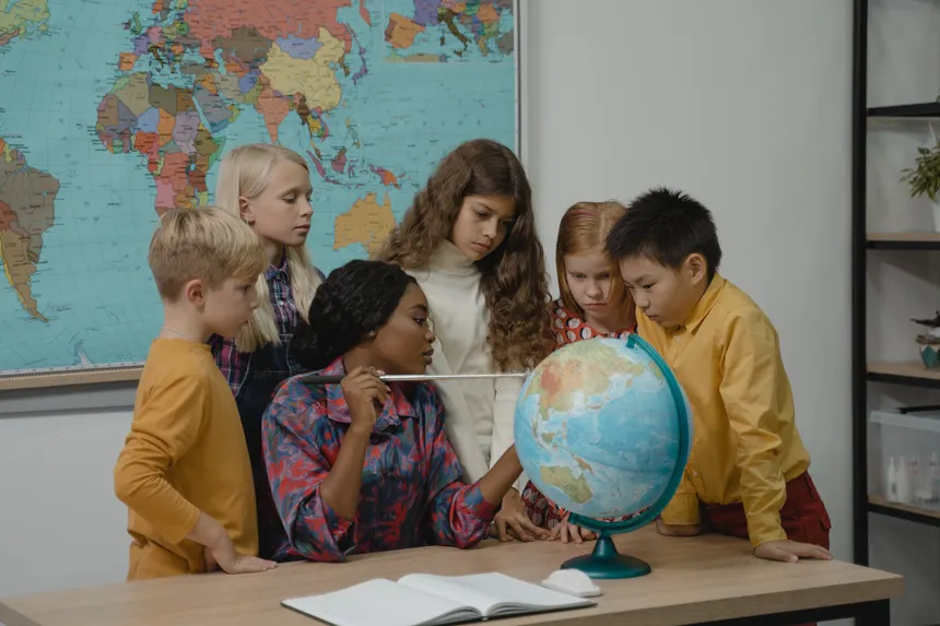 A diverse group of children learning geography with a teacher and globe in a classroom.