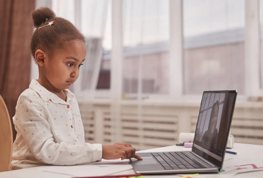 A focused child participating in a virtual class from home using a laptop.