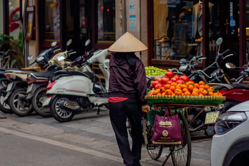 A Vietnamese street vendor pushes a fruit-laden bicycle through the bustling streets of Hanoi.