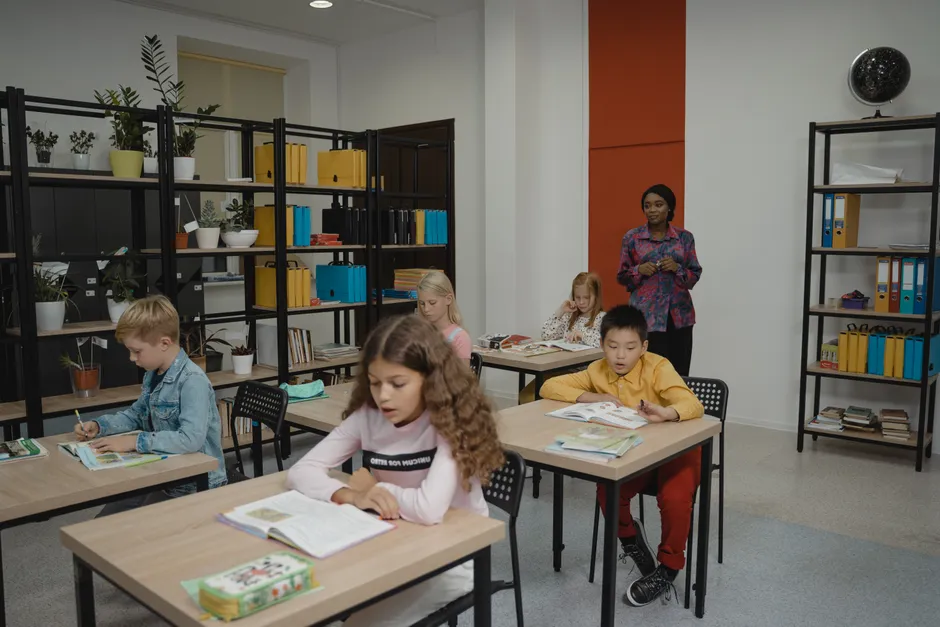 Elementary students focus on classwork with a teacher overseeing in a bright classroom.